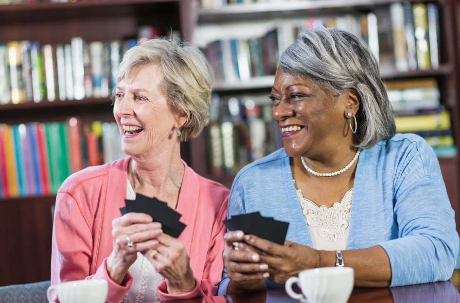 Two older adults play cards at the library.